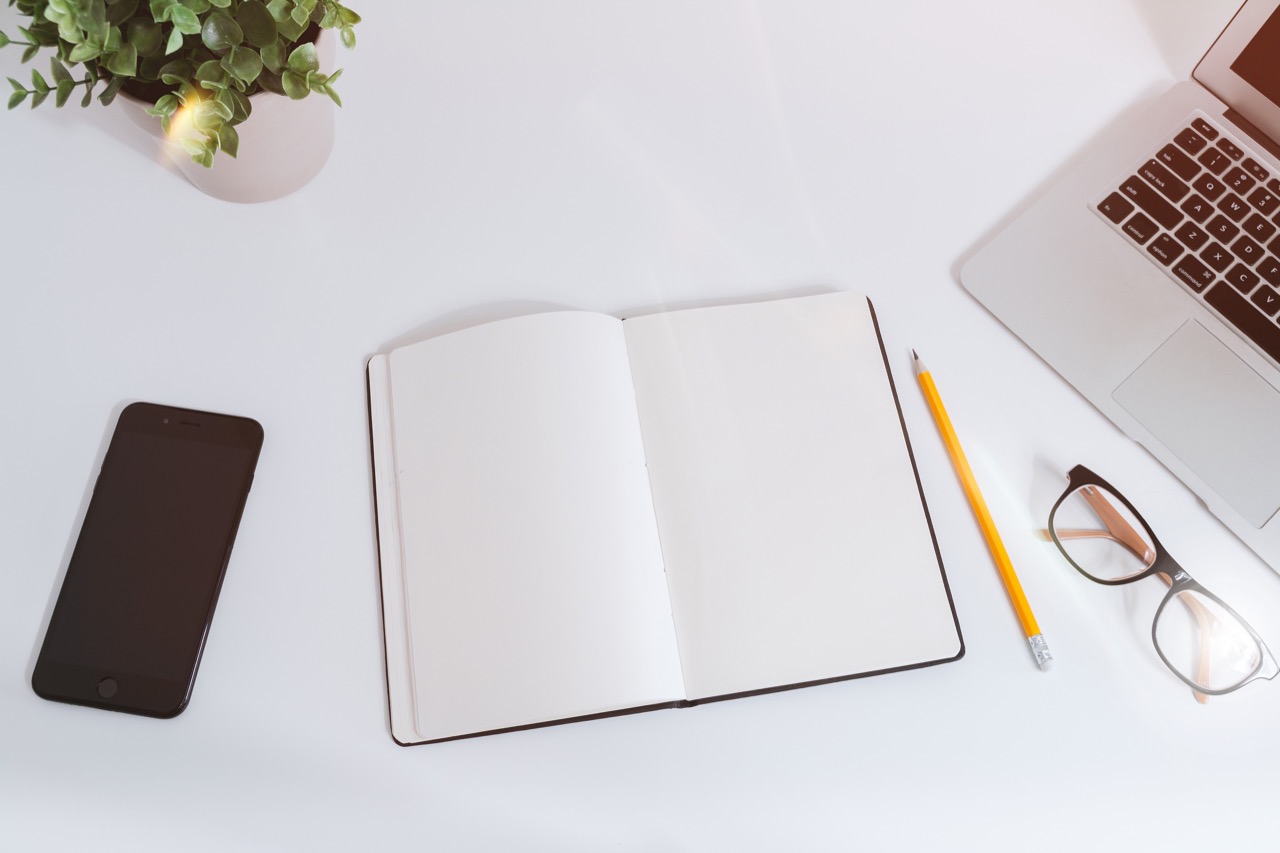 A notebook, phone, and laptop arranged on a work table